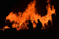 The photo presents people standing in front of a large fire.