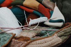 Colourful yarn, knitted textiles and knitting needles representing textile crafts and creative production.