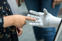 The photo presents a person interacting with a robotic hand.