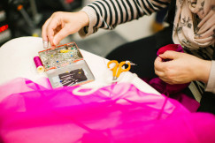 Person working with bright pink fabric alongside sewing needles, thread and scissors.
