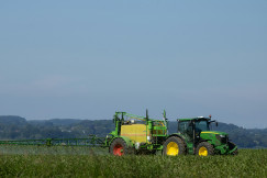 The photo presents a tractor spraying crops in a field.