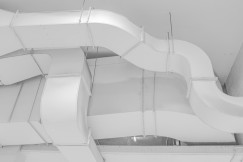 The picture presents large white ventilation ducts running across an industrial ceiling.
