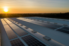 The photo presents solar panels on a large roof at sunset.
