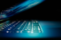 The photo presents a close-up of a laptop keyboard illuminated by blue light, symbolising digital technology and cybersecurity.