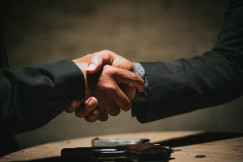 Two people shaking hands over a wooden table.
