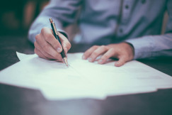 The photo presents a person signing a document.