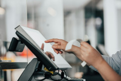 The photo presents a person using a touchscreen point-of-sale system while holding a receipt.