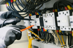 The picture describes a technician using testing probes to inspect electrical components inside an electrical control panel.