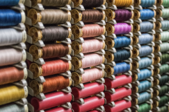 Rows of sewing thread spools arranged by colour, including shades of pink, blue, green, purple, grey and yellow.
