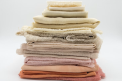 Stack of folded fabrics in pink, red, yellow, grey, and brown on a white surface. 