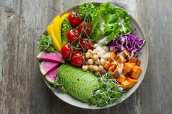The photo presents a colourful salad bowl with avocado, chickpeas, tomatoes, sweet potato, leafy greens, red cabbage and radish, topped with creamy dressing.