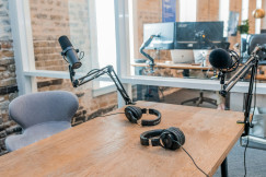 The photo presents a podcast recording setup with two microphones on adjustable arms and two pairs of headphones on a wooden table.