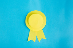 The photo presents a yellow paper award ribbon on a bright blue background.