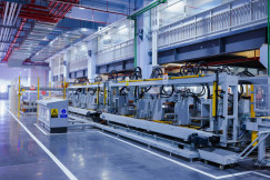 The photo presents an automated factory production line with rows of machinery, a control cabinet and yellow safety barriers.