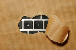 The photo presents torn brown paper revealing keyboard keys marked “A” and “I”, symbolising artificial intelligence.