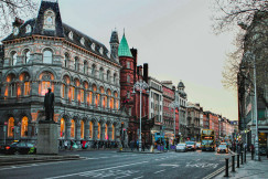 The photo presents a Dublin street lined with historic buildings, with double-decker buses, cars, pedestrians and a statue in the foreground.