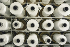 Rows of large white yarn cones stored on racks in a textile production facility.