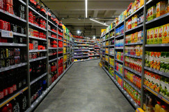The photo presents a supermarket aisle lined with shelves of soft drinks, juices, packaged foods and other groceries.