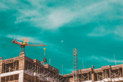 This picture shows a building under construction, featuring exposed concrete floors, scaffolding, and a tower crane lifting materials.