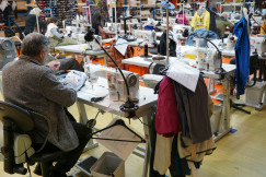 Man sewing at a machine in a busy workshop.