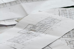 The picture shows several large architectural and engineering floor plans spread across a table