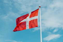 The photo presents the Danish flag waving against a blue sky.