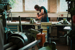 The photo presents a worker wearing safety glasses and ear protection using an angle grinder on metal, producing sparks in a workshop.
