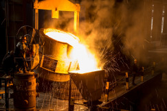 The photo presents workers pouring molten metal in a factory.