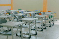 The picture shows an empty classroom with rows of desks and colorful chairs, representing educational infrastructure and modern learning environments.