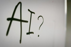 The photo presents the letters “AI” followed by a question mark, handwritten in black marker on a whiteboard.