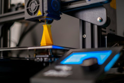 The photo presents a 3D printer creating a yellow object.