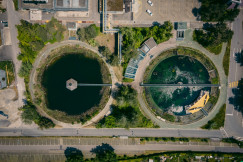 The photo presents an aerial view of a water treatment facility with circular settling ponds, pipelines, surrounding greenery and nearby roads.