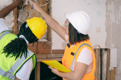 The picture describes two construction workers inspecting and installing electrical wiring inside a building under renovation.