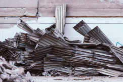 The picture describes a pile of demolished corrugated metal sheets stacked against a damaged industrial wall.