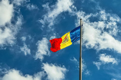 The photo presents the Moldovan flag flying on a tall pole against a blue sky with white clouds.