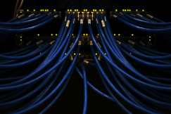 The photo presents blue Ethernet cables connected to network switches, with glowing indicator lights in a dark equipment rack.