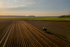 The photo presents a tractor working in a brown field.