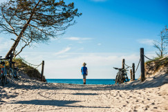 The photo presents a child walking along a sandy path towards the sea.