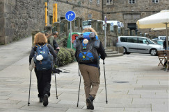 The photo presents two hikers with backpacks and walking poles walking along a stone-paved street.