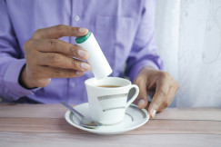 The photo presents a person adding sweetener to a cup of tea.