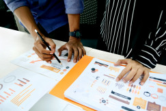 The photo shows two people reviewing charts and infographics at a table.