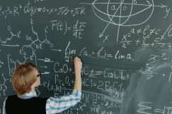 The photo presents a person writing mathematical and chemical equations on a large chalkboard.