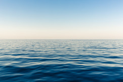 The photo presents a calm blue sea with gentle ripples stretching to the horizon beneath a clear sky.