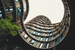 This picture captures a modern architectural courtyard viewed from below, looking upward toward the sky through the centre of a curved building.