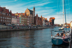 The photo presents the historic waterfront of Gdańsk, Poland, with the Motława River and the medieval Crane in the background.