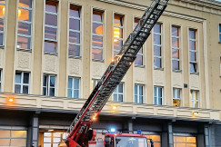 This picture shows a firefighting ladder truck positioned outside a large building, with its telescopic aerial ladder fully extended toward the upper floors.
