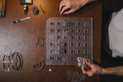 The picture shows a top-down view of an architectural design or model-making workspace, with a person working on transparent components.