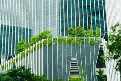 The picture shows a modern building with glass façades, distinctive white structural elements, and lush greenery integrated across terraces and balconies.