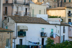 The picture shows traditional Italian buildings with tiled roofs, balconies, weathered façades, palm trees, and laundry hanging outside.