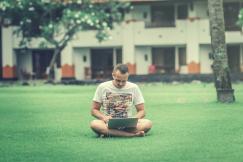 An illustrative photo of a man sitting on ground while using smartphone